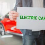 Młoda rodzina kupuje pierwszy samochód elektryczny w salonie. Zbliżenie: trzymając się za ręce papier ze słowem Samochód elektryczny. Ekologiczny samochód elektryczny na baterie dla ochrony środowiska.