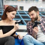 Portret wesołej, aktywnej pary grającej w gry wideo na playstation z kontrolerem konsoli w dłoniach, fani Xboxa