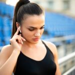 wysportowana dziewczyna pozuje na stadionie i słucha muzyki przez słuchawki