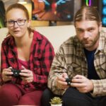 Focused couple playing online video games sitting on couch in living room. Playing games using wireless controllers.