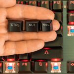 męska ręka trzyma na dłoni trzy klawisze - ctrl alt del nad czarną podświetlaną klawiaturą