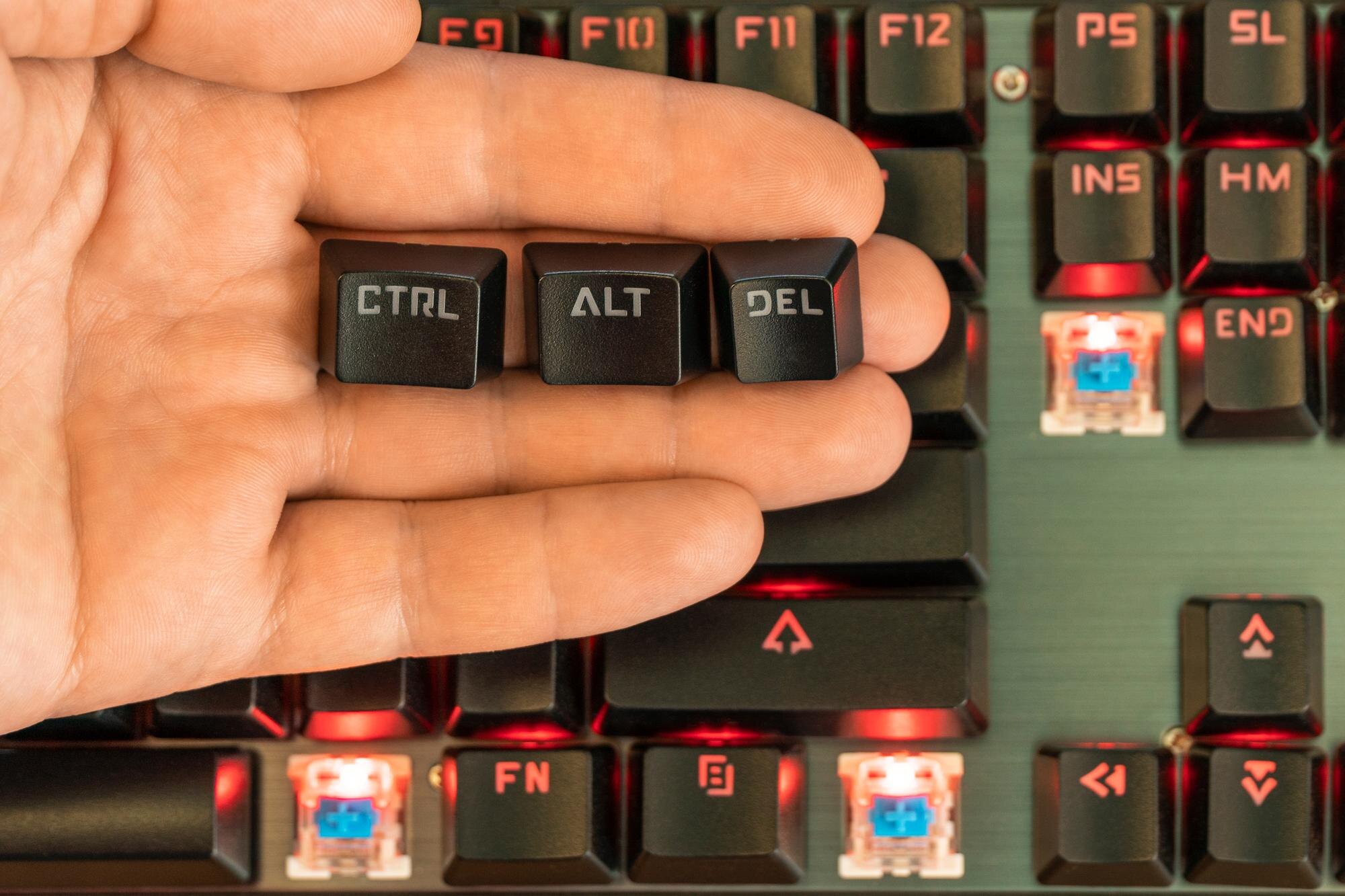 męska ręka trzyma na dłoni trzy klawisze - ctrl alt del nad czarną podświetlaną klawiaturą