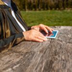 Ręce starszej kobiety trzymającej tablet na świeżym powietrzu w ciepły letni dzieńZbliż selektywne skupienie