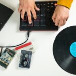 Ręce mężczyzny tworzącego muzykę na swoim kontrolerze MIDI kontrastują ze starymi winylami i kasetami, z których sampluje