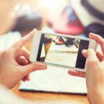 koncepcja wakacji, turystyki, podróży, technologii i ludzi - zbliżenie kobiety ze smartfonem fotografującej mapę i rzeczy podróżne